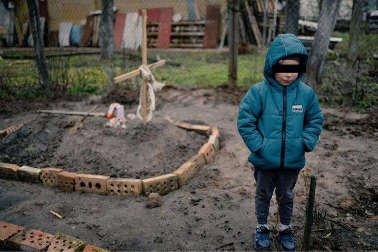 Imagine-simbol a crimelor lui Putin în Ucraina: Un copil de 6 ani așteptă lângă mormântul mamei sale